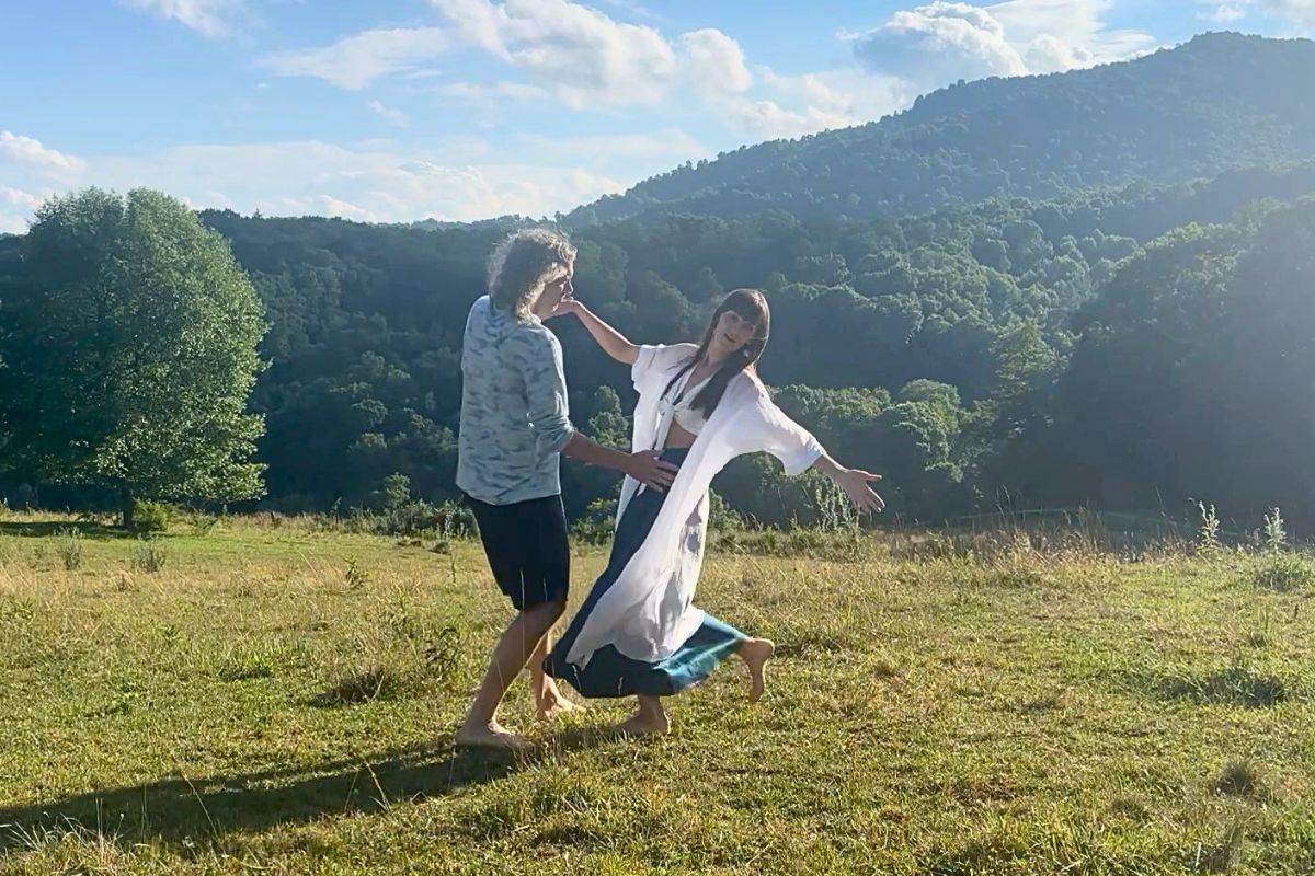 Gita and Matt dancing together in a sunlit meadow with green hills behind them