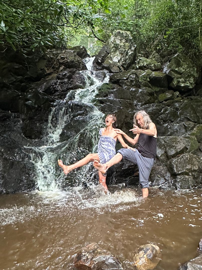Two people laughing beneath a forest waterfall