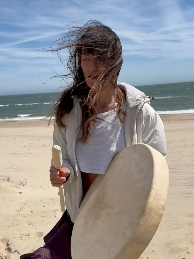 Person holding a frame drum on a windswept beach