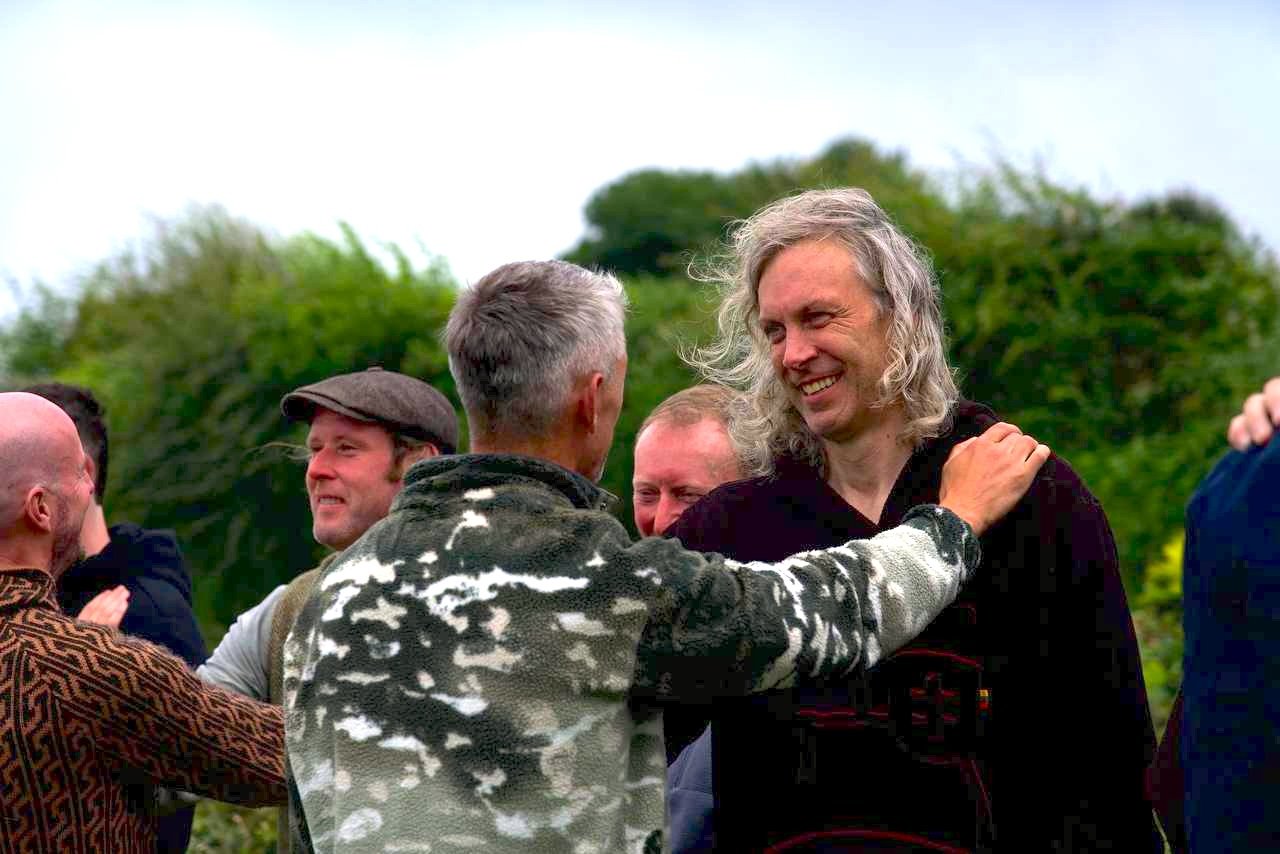 Matt smiling as he is embraced in a circle of men outdoors